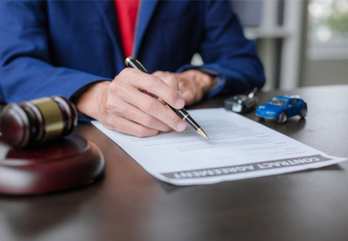 Attorney signing a contract related to comparative negligence, with gavel and toy car symbolizing accident law