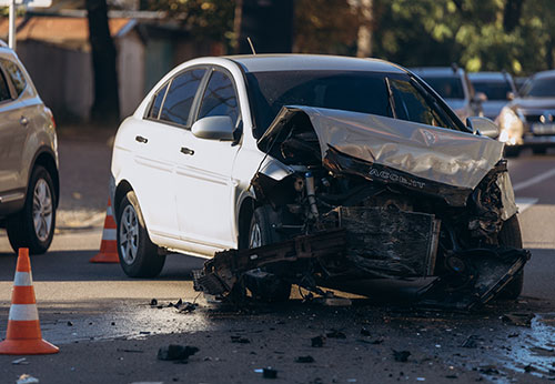 Crashed white car with severe front-end damage on a street, symbolizing accident claims for residents