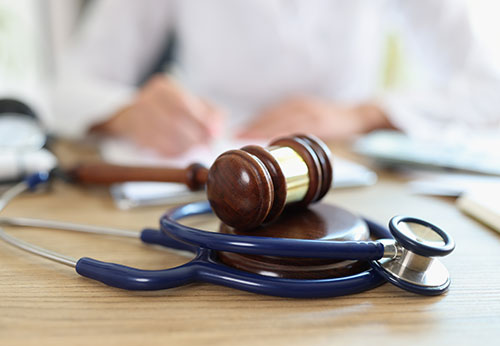 Medical malpractice lawyer reviews documents with a gavel and stethoscope on a wooden desk