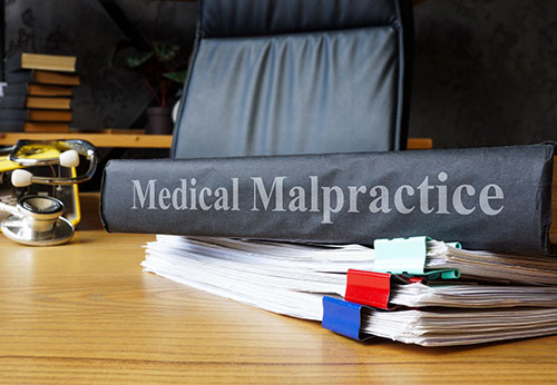 Folder labeled Medical Malpractice on a stack of documents with office chair, symbolizing legal support